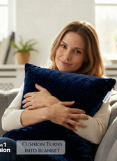 Woman holding a blue cushion with blanket feature, sitting on a couch in a bright room.